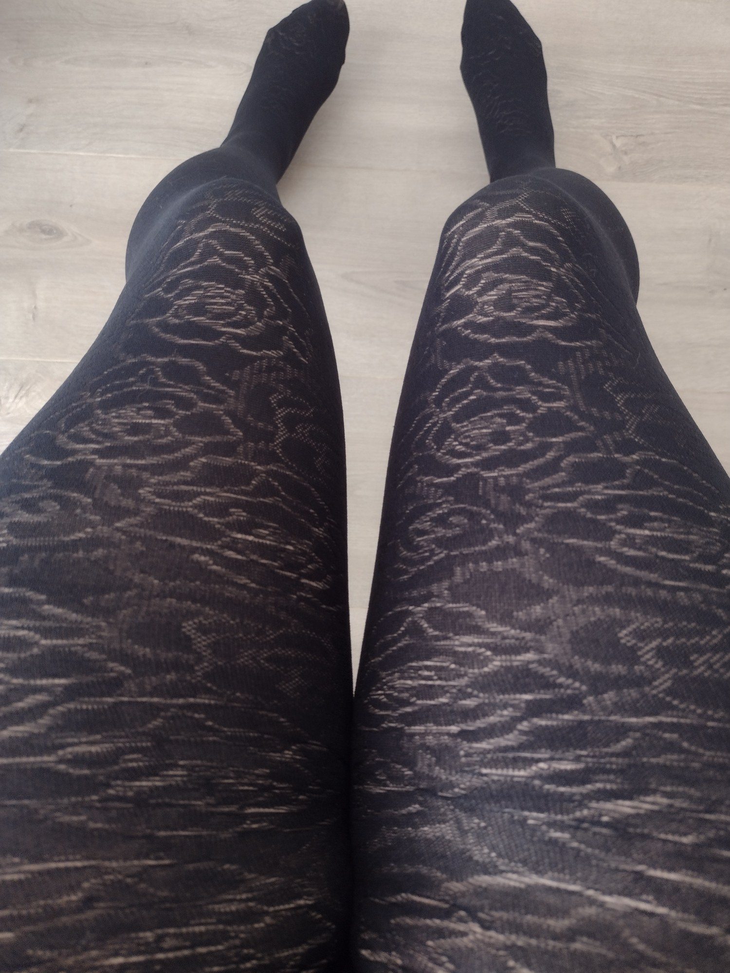 Black opaque tights with a bold rose floral jacquard knit pattern, worn on legs