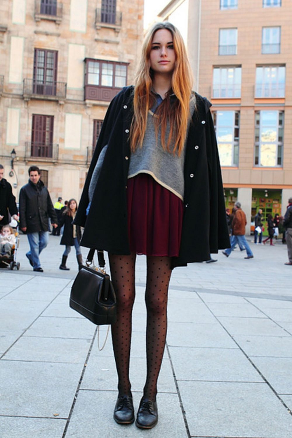 Burgundy skirt with black cape coat and black polka dot tights in a city square