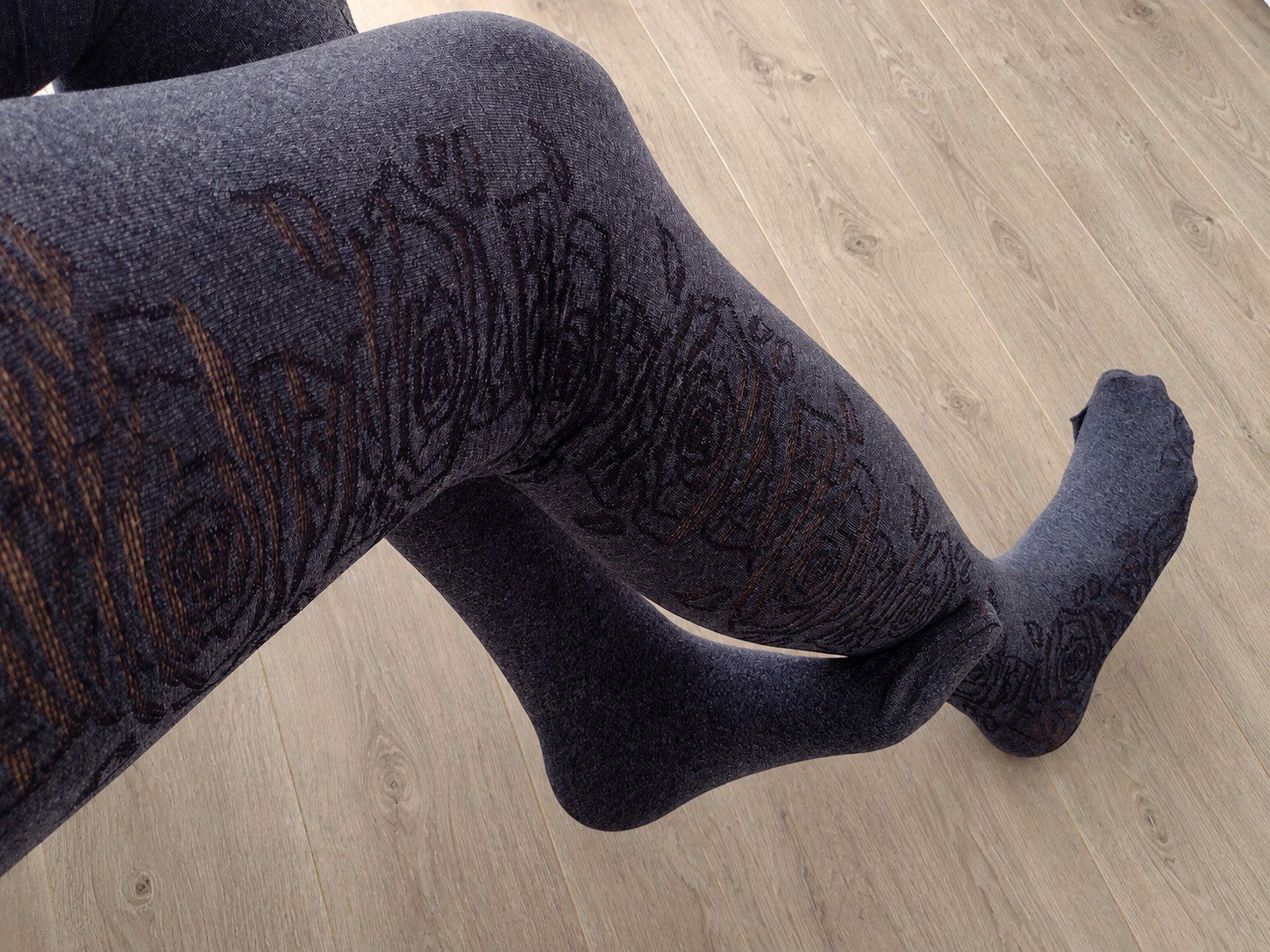 Charcoal grey opaque tights with a black rose floral jacquard pattern, worn on legs, retouched background
