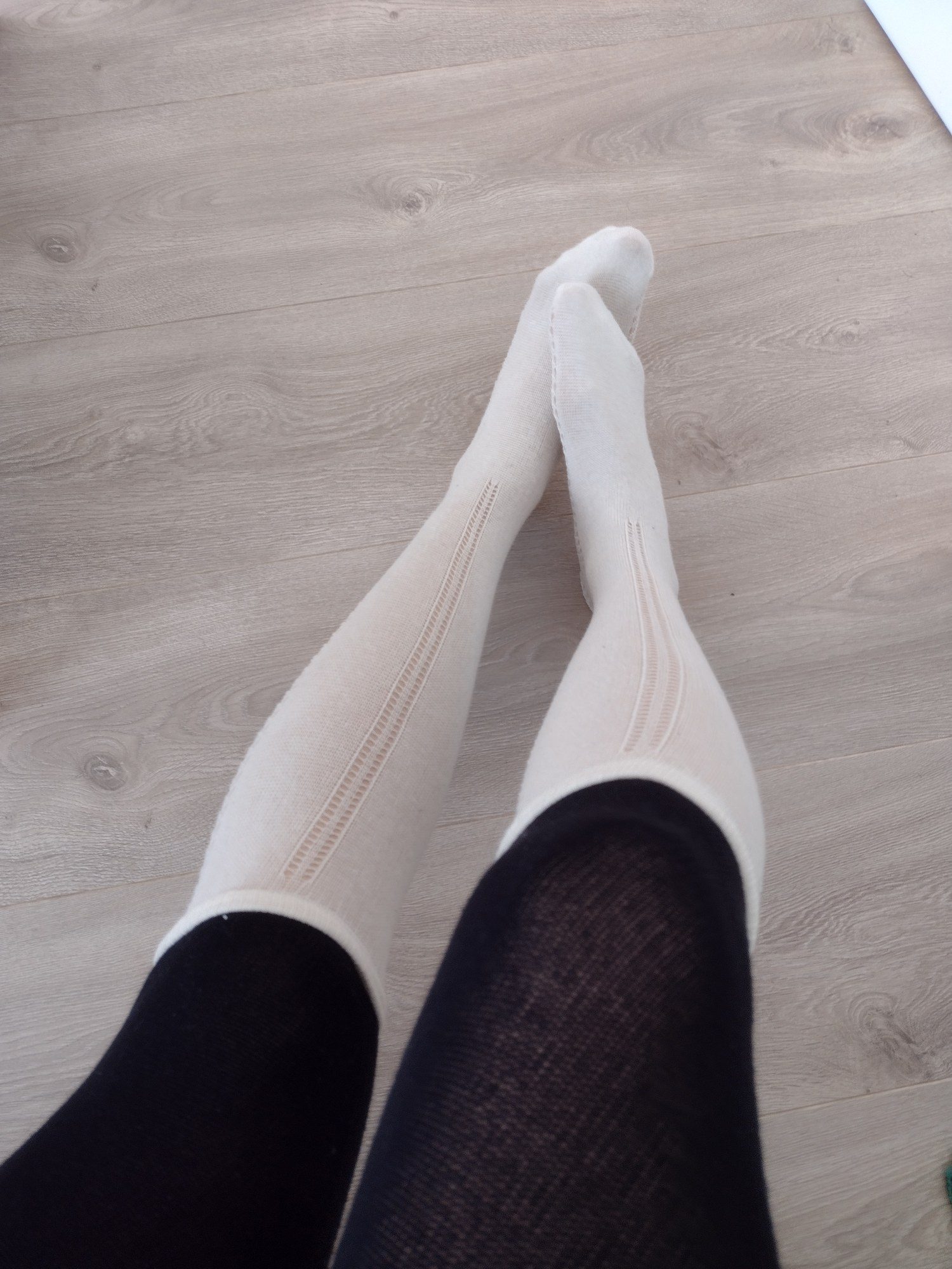 Ivory ribbed knit foot and calf transitioning into black fishnet pantyhose, worn, bold two-tone contrast