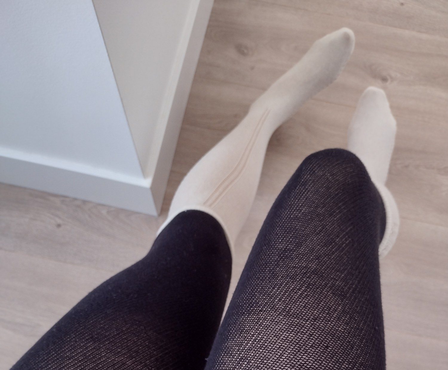 Close-up of ivory ribbed knit feet and calves transitioning into black fishnet, cropped above the thigh