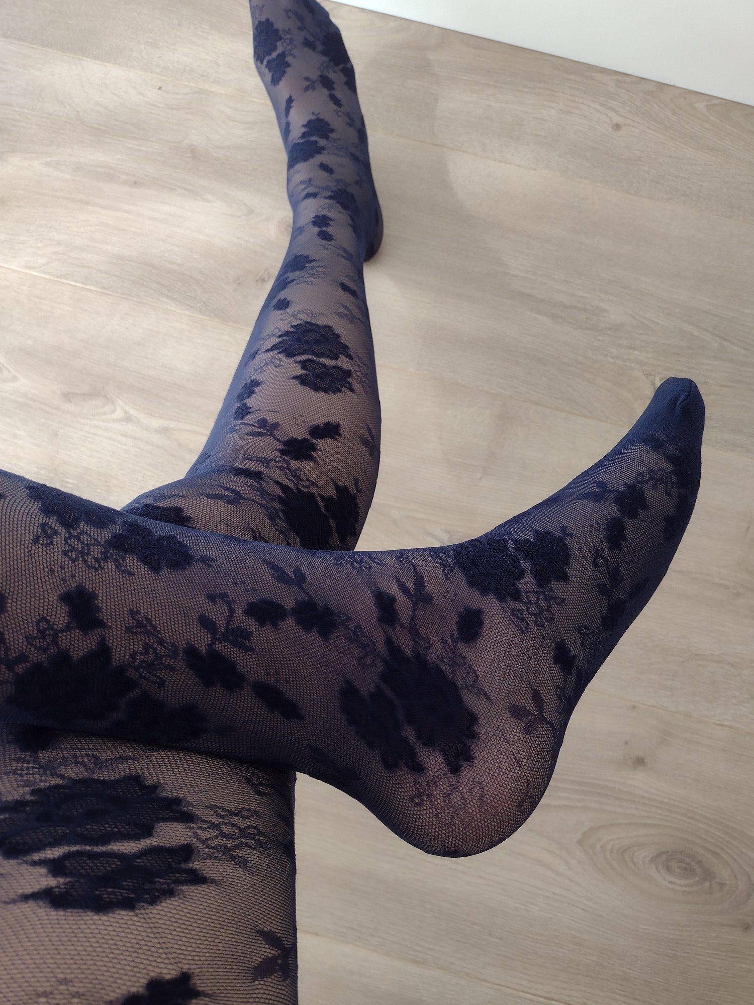 Full leg view of navy sheer tights with a black floral lace pattern