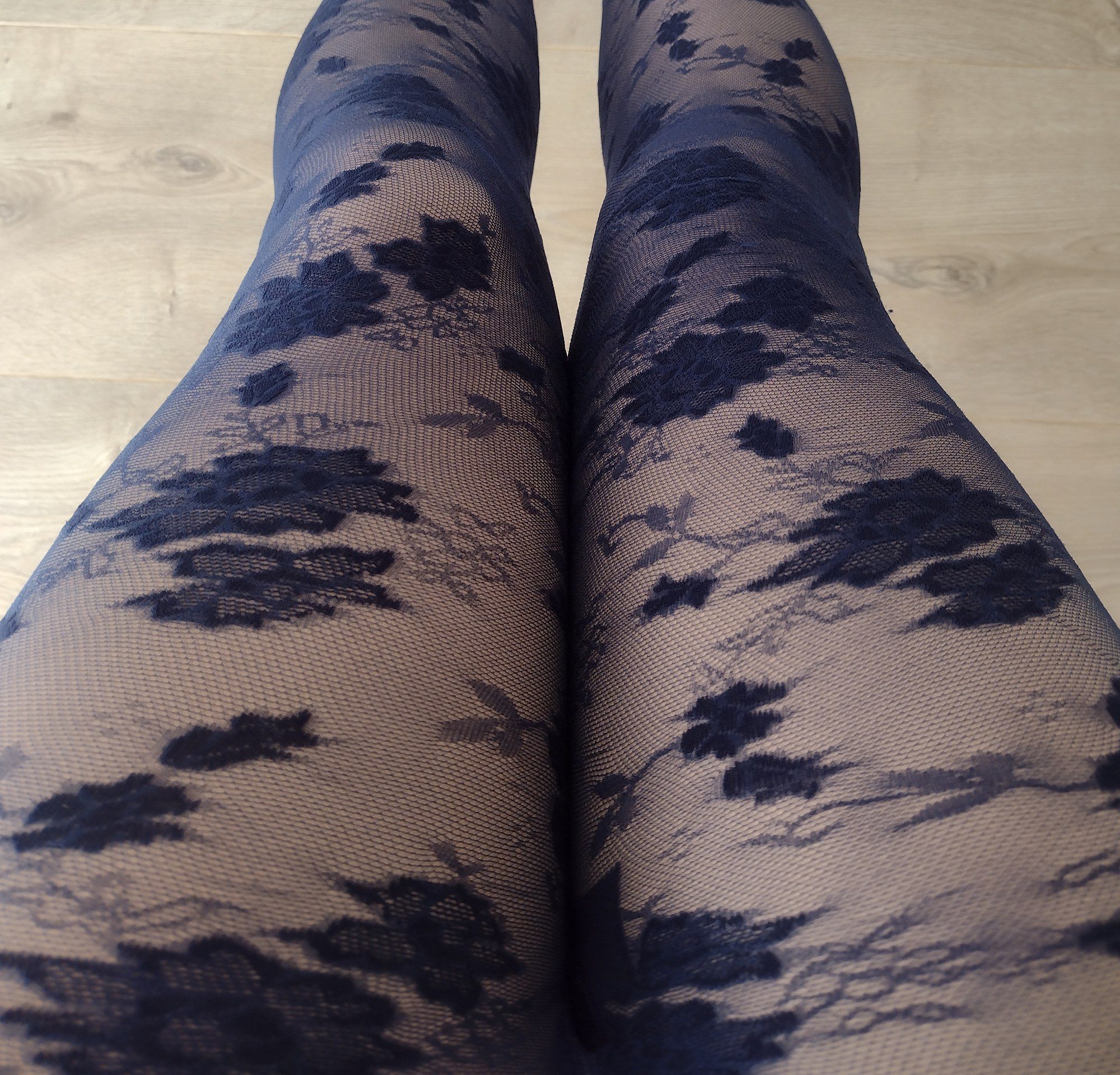 Close-up of navy sheer floral lace tights showing the print detail on both knees