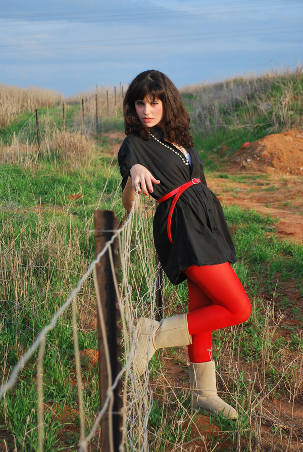 Bright red tights with a black shift dress, red belt and beige shearling boots, worn outdoors by a fence