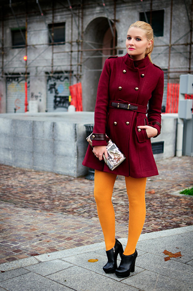 Bright yellow tights with a burgundy military-style coat, black ankle boots, and a printed clutch