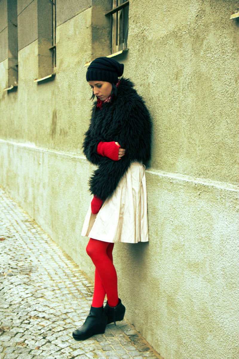 Bright red tights with matching red fingerless gloves, a black faux-fur jacket and cream pleated skirt