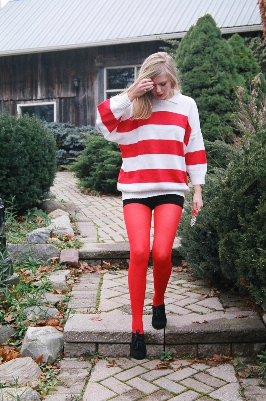 Bright red tights with an oversized red and white striped sweater and black shorts, walking on a path near a barn