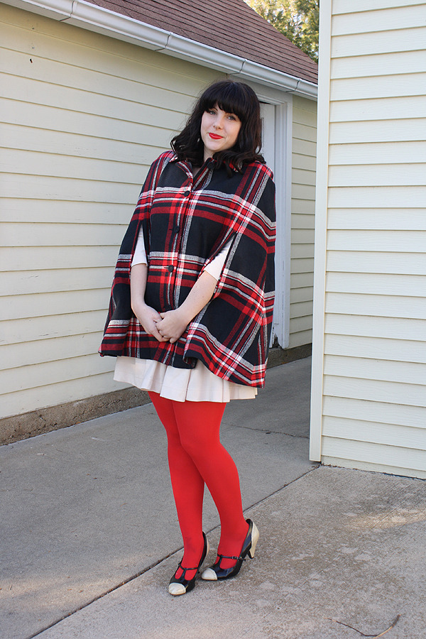 Bright red tights with a red black and white tartan cape, white pleated skirt, and black t-strap heels