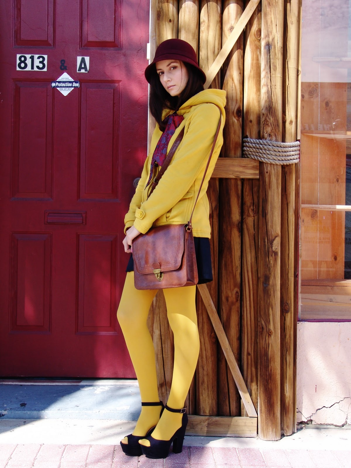 Bright yellow opaque tights with a matching yellow hooded jacket, burgundy cloche hat and scarf, and black platform sandals