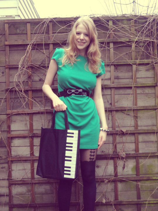 Black faux thigh-high tights with a sheer bow-print top, worn with a green mini dress, black belt and a piano-key tote bag