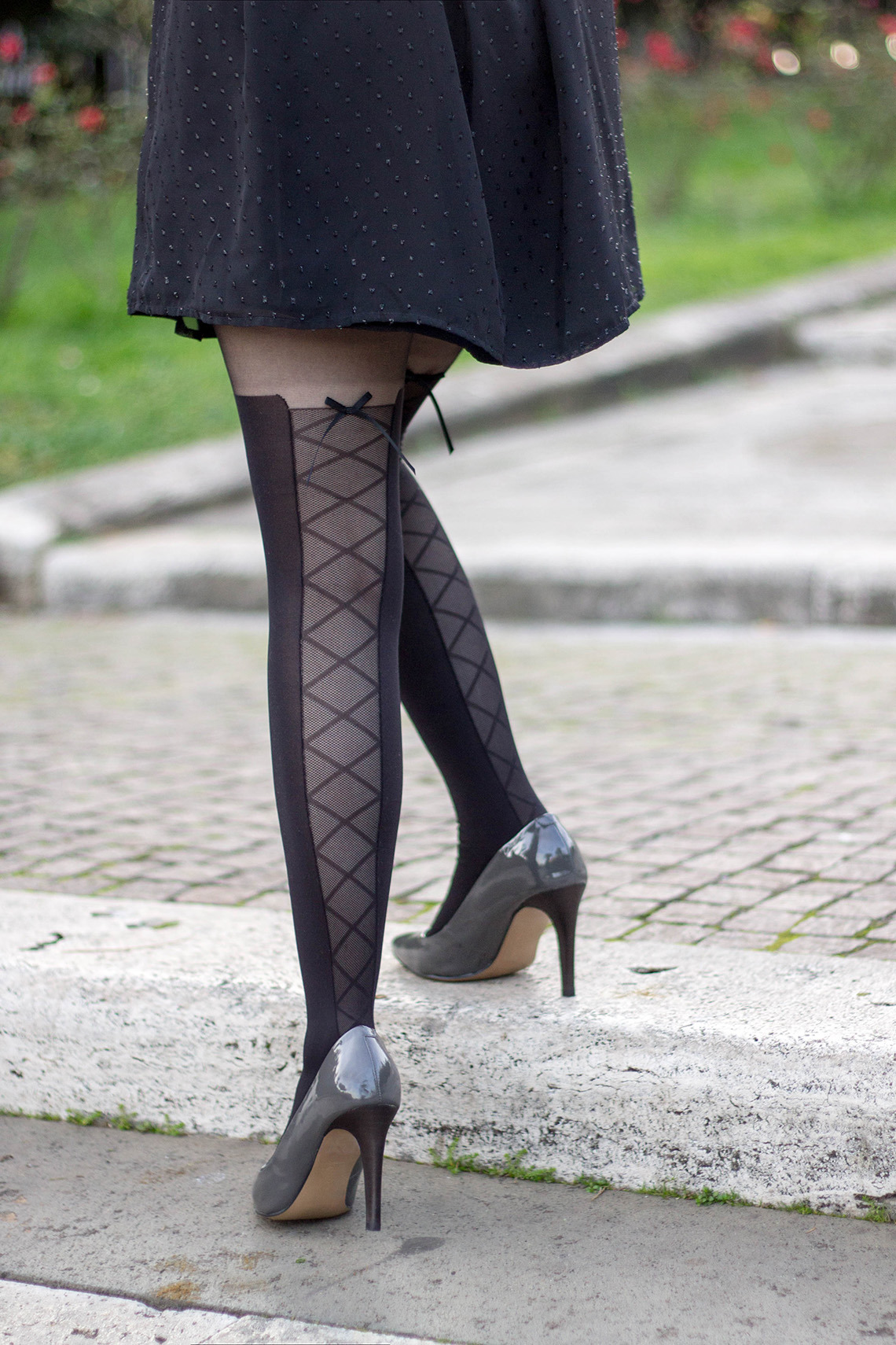 Black faux thigh-high tights with a diamond lattice back panel and bow, worn with a black swiss-dot dress and grey pumps