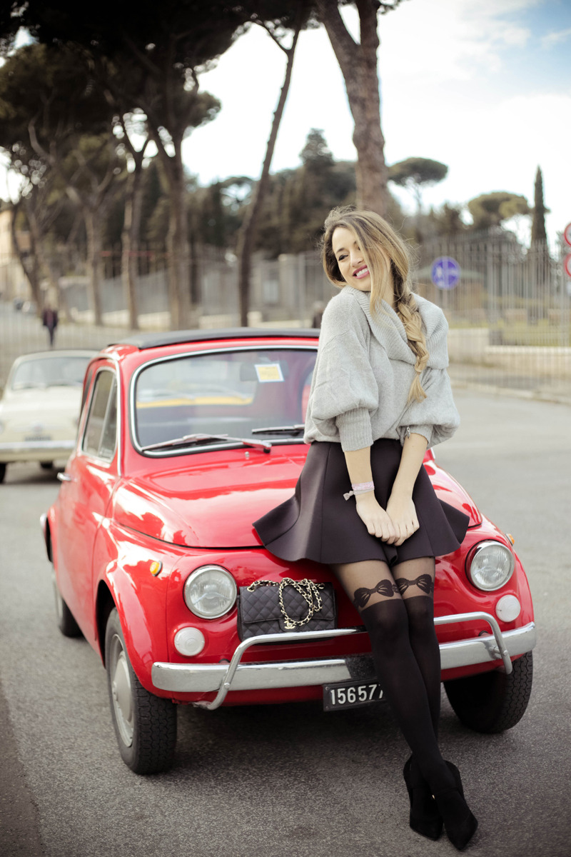 Tonal black bow-print faux thigh-high tights with an oversized grey sweater and flared mini skirt