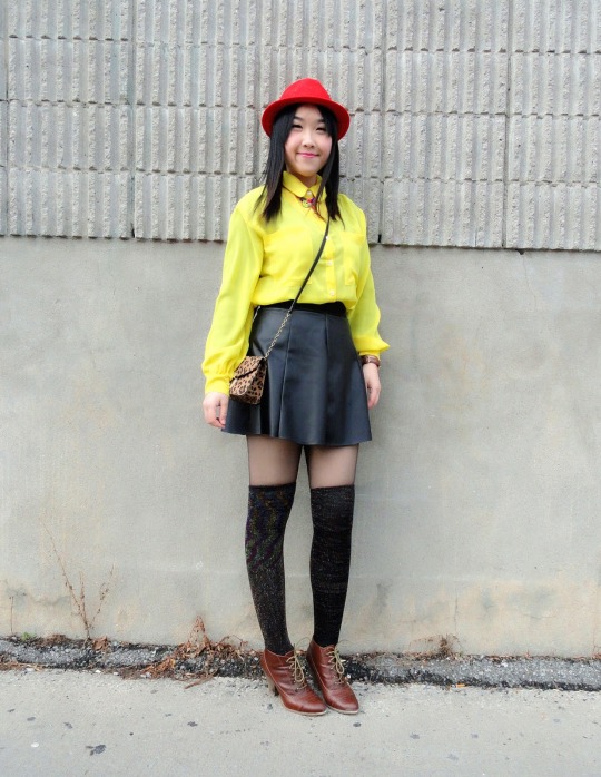 Dark textured faux thigh-high tights with a sheer top band, worn with a bright yellow blouse, a black leather-look skater skirt, a red fedora and brown lace-up booties