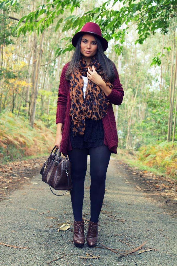Navy tights with dark oxblood leather ankle boots, a burgundy cardigan, a felt hat and a leopard print scarf in a forest