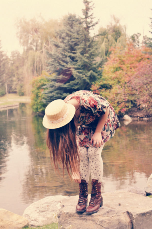 Cream dotted tights with dark brown leather lace-up boots, a floral dress and a straw boater hat by a lake