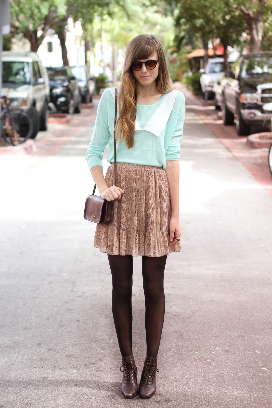 Black tights with dark brown leather lace-up booties, a beige pleated skirt and a mint top on a city street