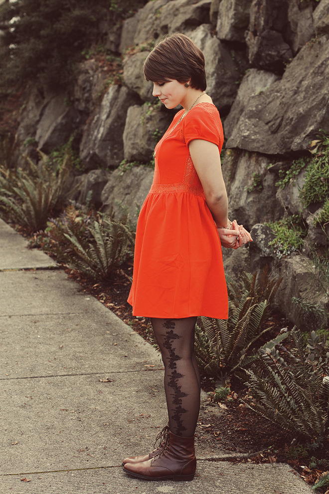 Black lace tights with a fine vine pattern and dark brown leather lace-up boots, with a bright orange dress