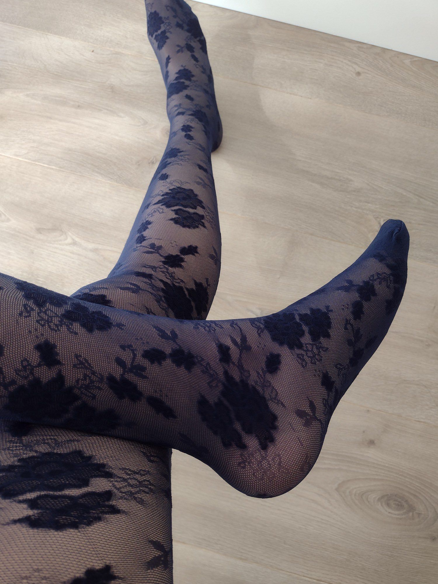 Full leg view of navy sheer tights with a black floral lace pattern