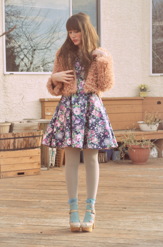 Woman in cream tights with pale blue platform sandals and frilly socks, wearing a floral dress and peach jacket