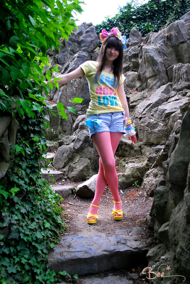 Woman in pink tights with yellow bow platform sandals and denim shorts, with a graphic tee on rocky steps