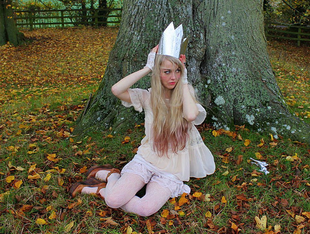 Woman in white lace tights with brown ankle boots and a cream lace dress, sitting under a tree wearing a paper crown