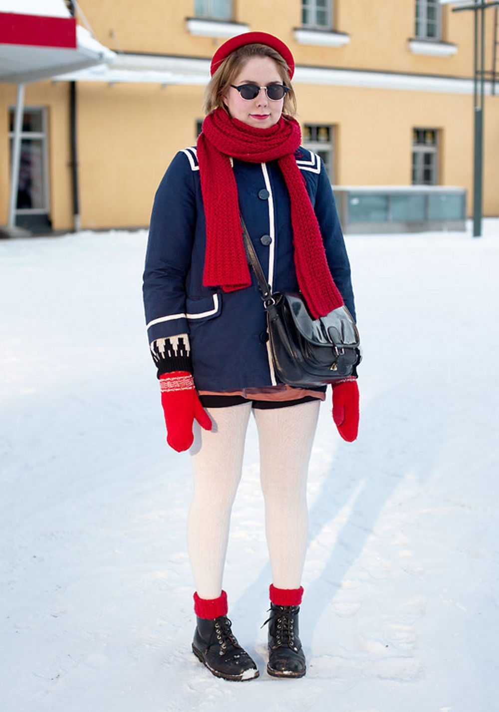 Woman in white opaque tights with black boots and red socks, wearing a navy coat, red scarf and red mittens in the snow