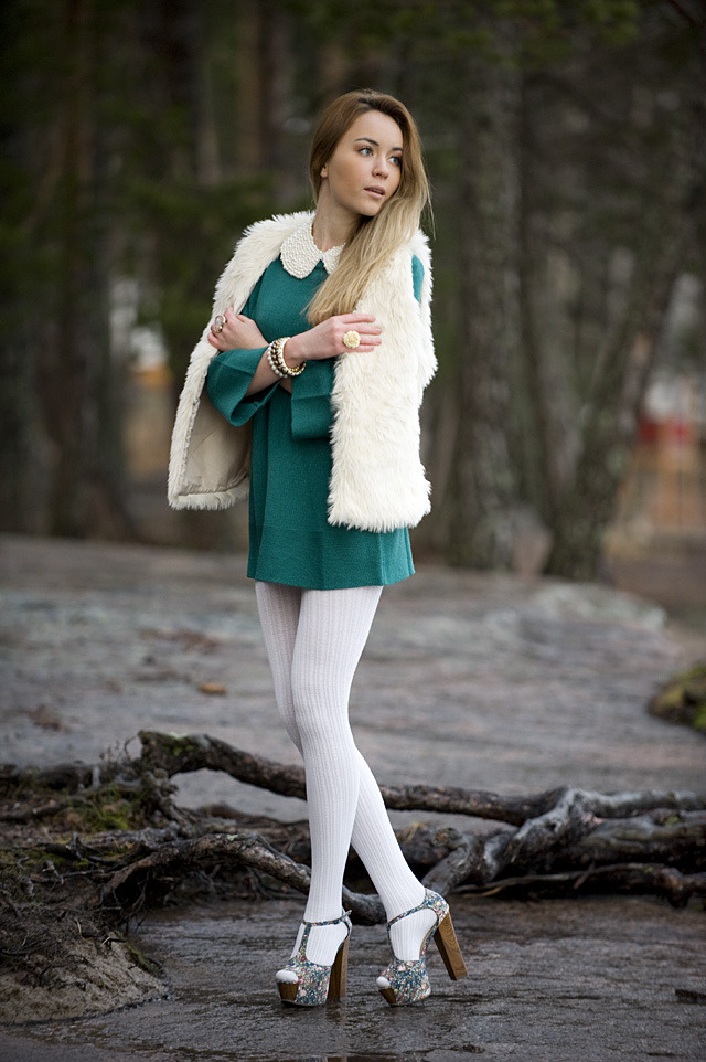 Woman in white ribbed tights with silver glitter platform sandals and a teal dress, with a cream faux fur vest