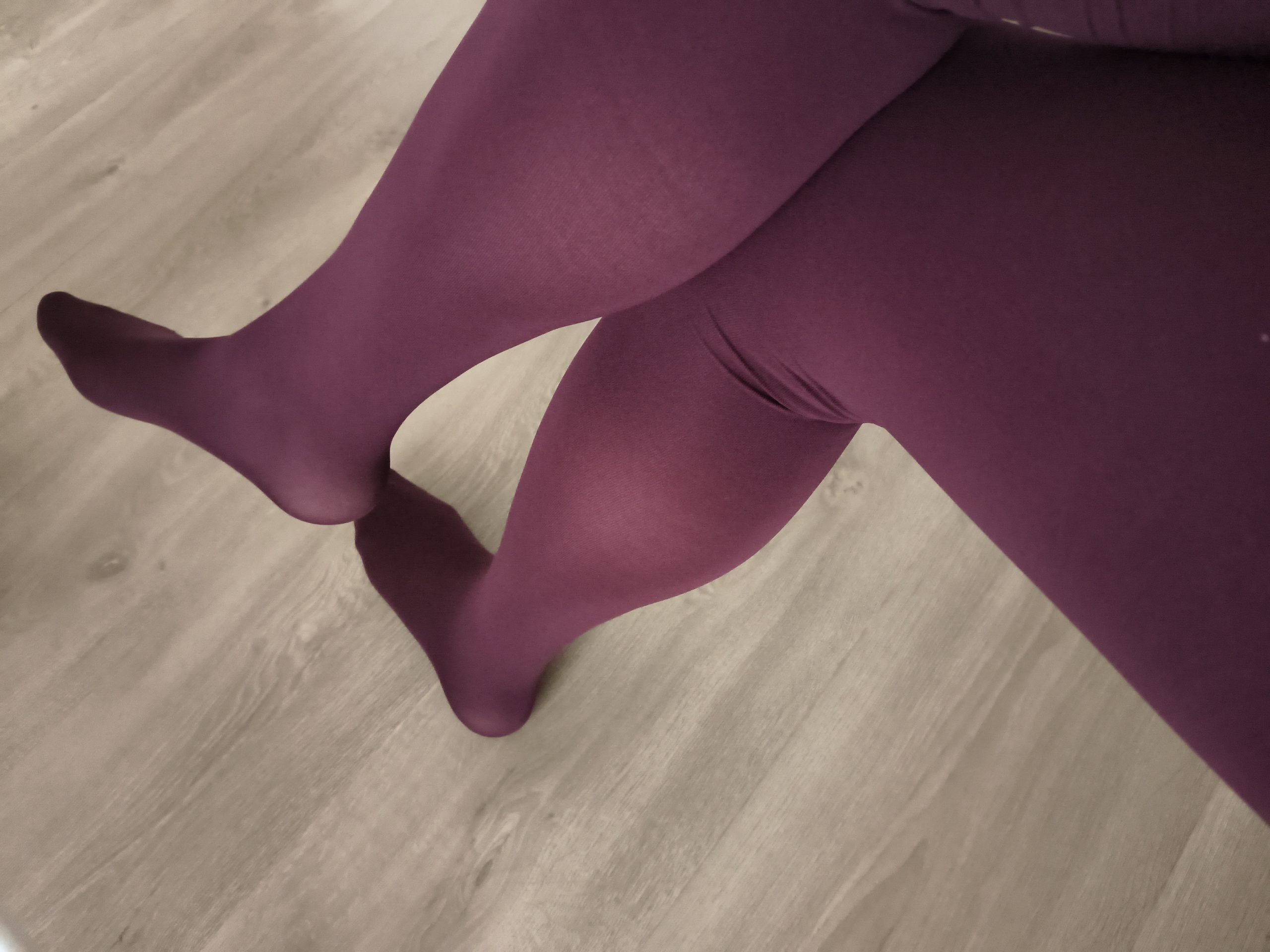 Woman in Yirane burgundy 80D opaque tights, legs crossed at the ankle, on a wooden floor